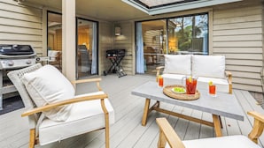 An outdoor patio with a table and chairs, a grill, and a sliding glass door leading to a covered area. - 112 The Greens @ Shipyard | Golf, Tennis &  Pool | Walk to Beach (Hilton Head Island)
