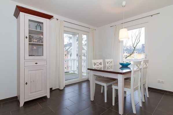 A dining area with a table and chairs, a cabinet with glass doors, and a view through a sliding glass door to the outside.
