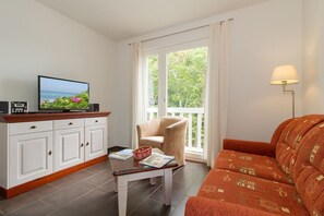 A living room with a television, a sofa, a coffee table, and a window with curtains. - Ferienwohnung W18.2.s - 3-zimmer-ferienwohnung für 4 Pers. im 2. Obergeschoss, Strandnah mit Wlan (Graal-Müritz)