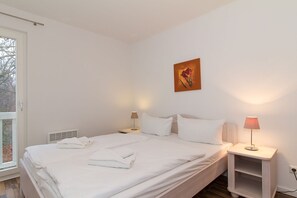 A bedroom with a bed, two bedside tables, a window, and a painting on the wall.