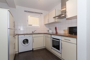 A compact kitchen with a washing machine, oven, and a coffee maker.