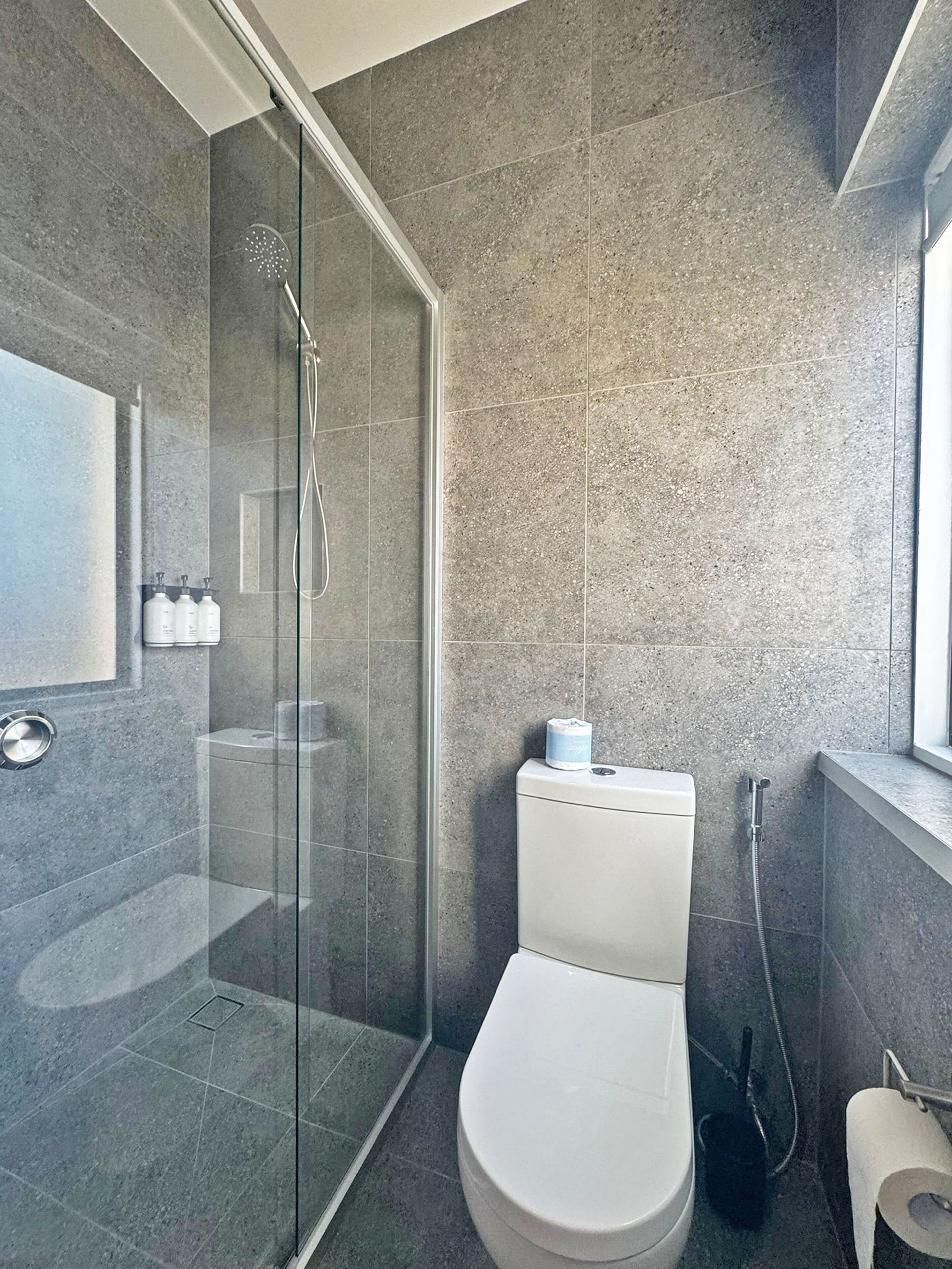 Un baño moderno con ducha envuelta en vidrio, inodoro y un espejo grande.