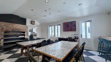 A spacious room with a large table and chairs, a brick fireplace, and a kitchen area.