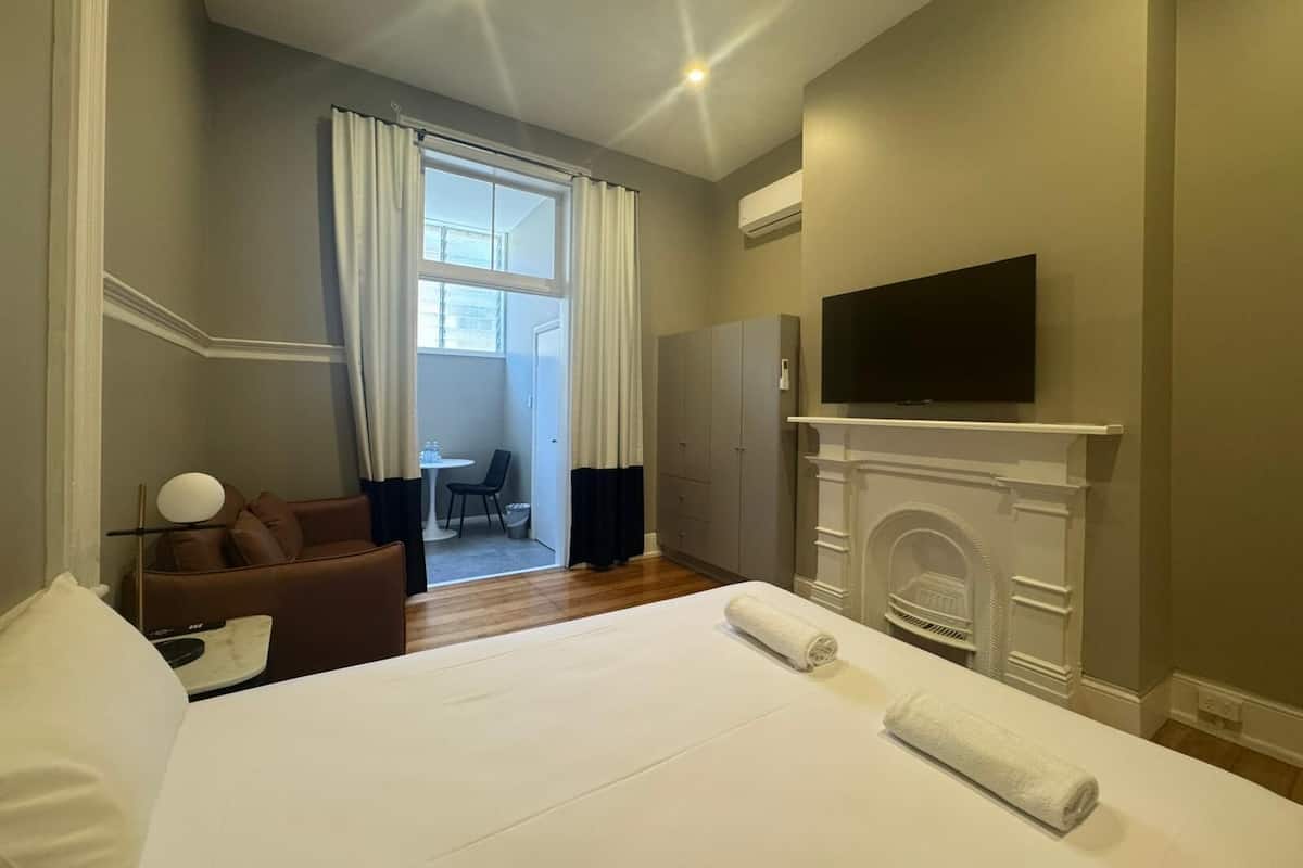 Habitación de hotel con cama, televisor sobre la chimenea, escritorio con silla y vista al balcón exterior a través de una ventana.