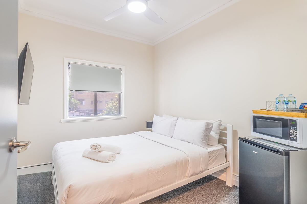 Un dormitorio con cama, microondas, refrigerador, ventana y puerta.