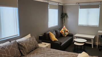 A hotel room with a large bed, a sofa, a small table, and a ceiling fan.