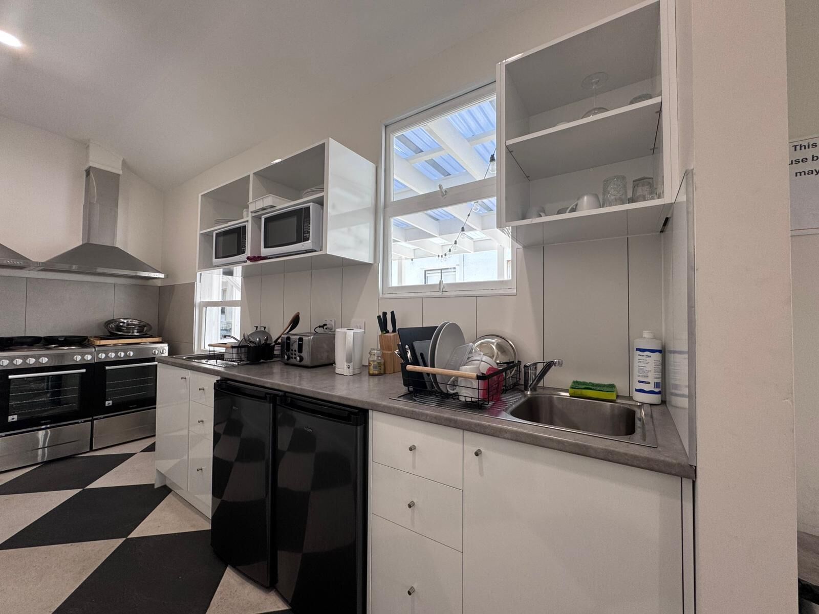 A modern kitchen with white cabinets, a black and white checkered floor, a built-in oven, a microwave, a toaster, and a sink.