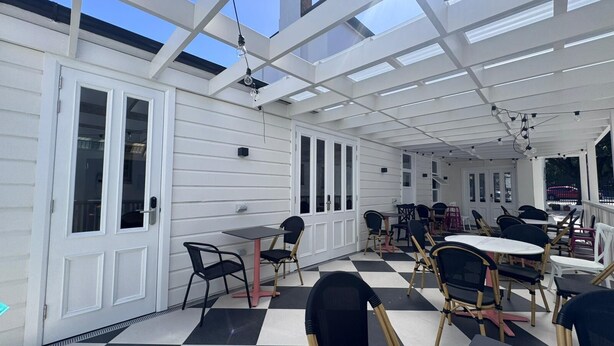 An outdoor patio with a checkered floor, white walls, and multiple tables and chairs. - K2 Brisbane (Spring Hill)