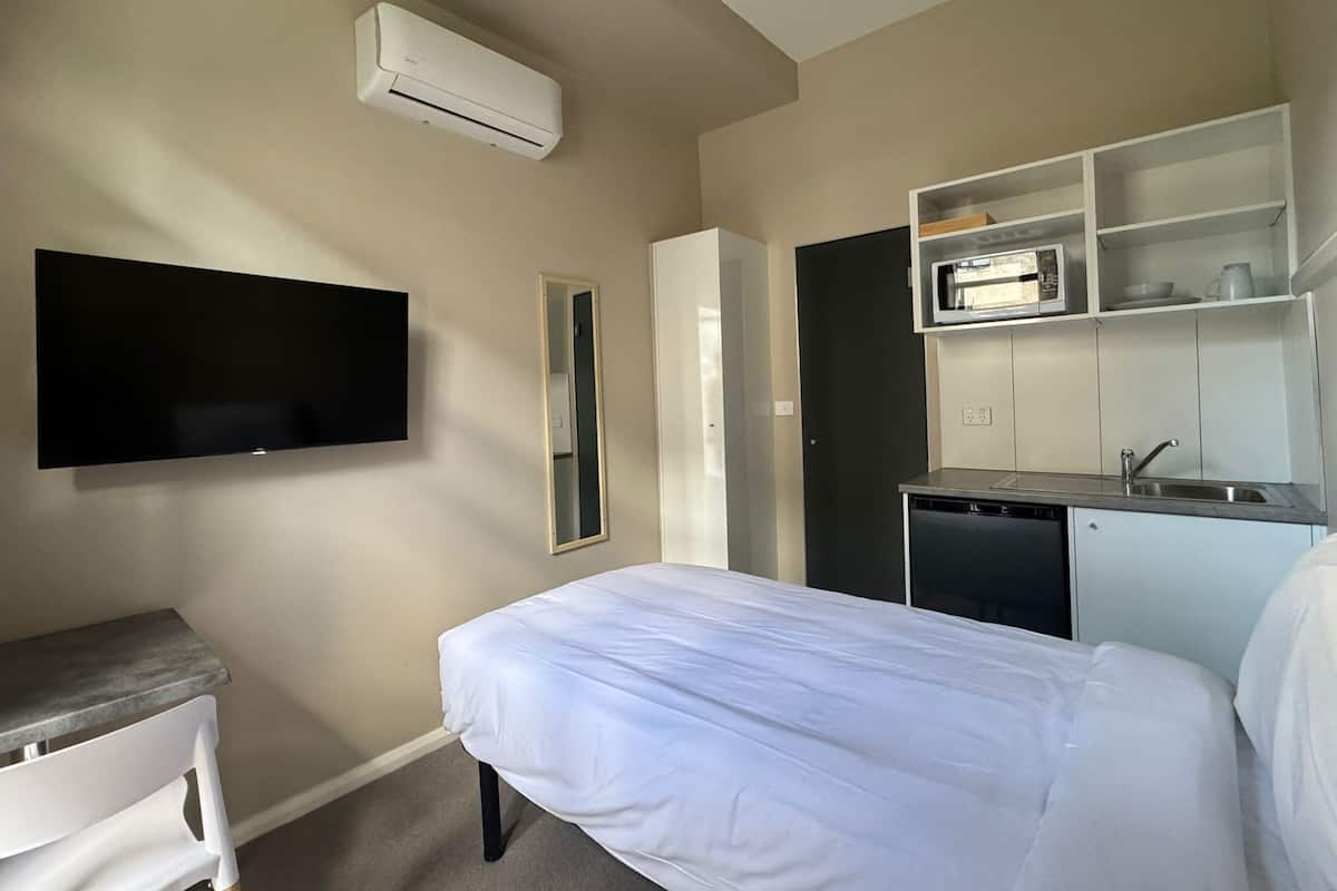Una habitación de hotel con cama, televisión, kitchenette pequeño y espejo.
