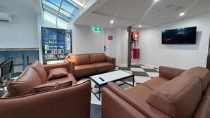 A modern lobby with leather sofas, a vending machine, a fire extinguisher, and a television. - K2 Brisbane (Spring Hill)