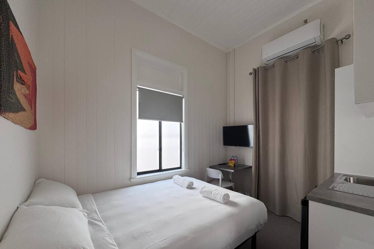 Habitación de hotel con cama, escritorio con silla, televisor y ventana con cortinas.