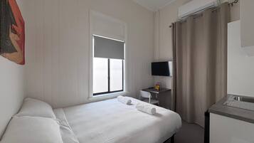 Une chambre d’hôtel avec un lit, un bureau et une chaise, une télévision et une fenêtre avec des rideaux.