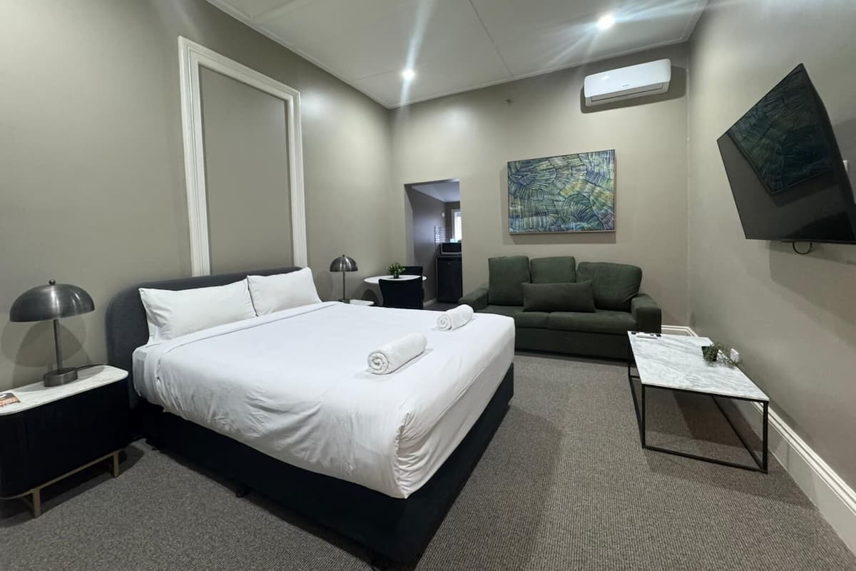 Una habitación de hotel con cama, sofá, una mesita, televisor y aire acondicionado.