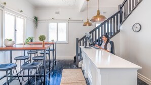 A kitchen with a wooden table, bar stools, and a person at the counter. - K2 Brisbane (Spring Hill)