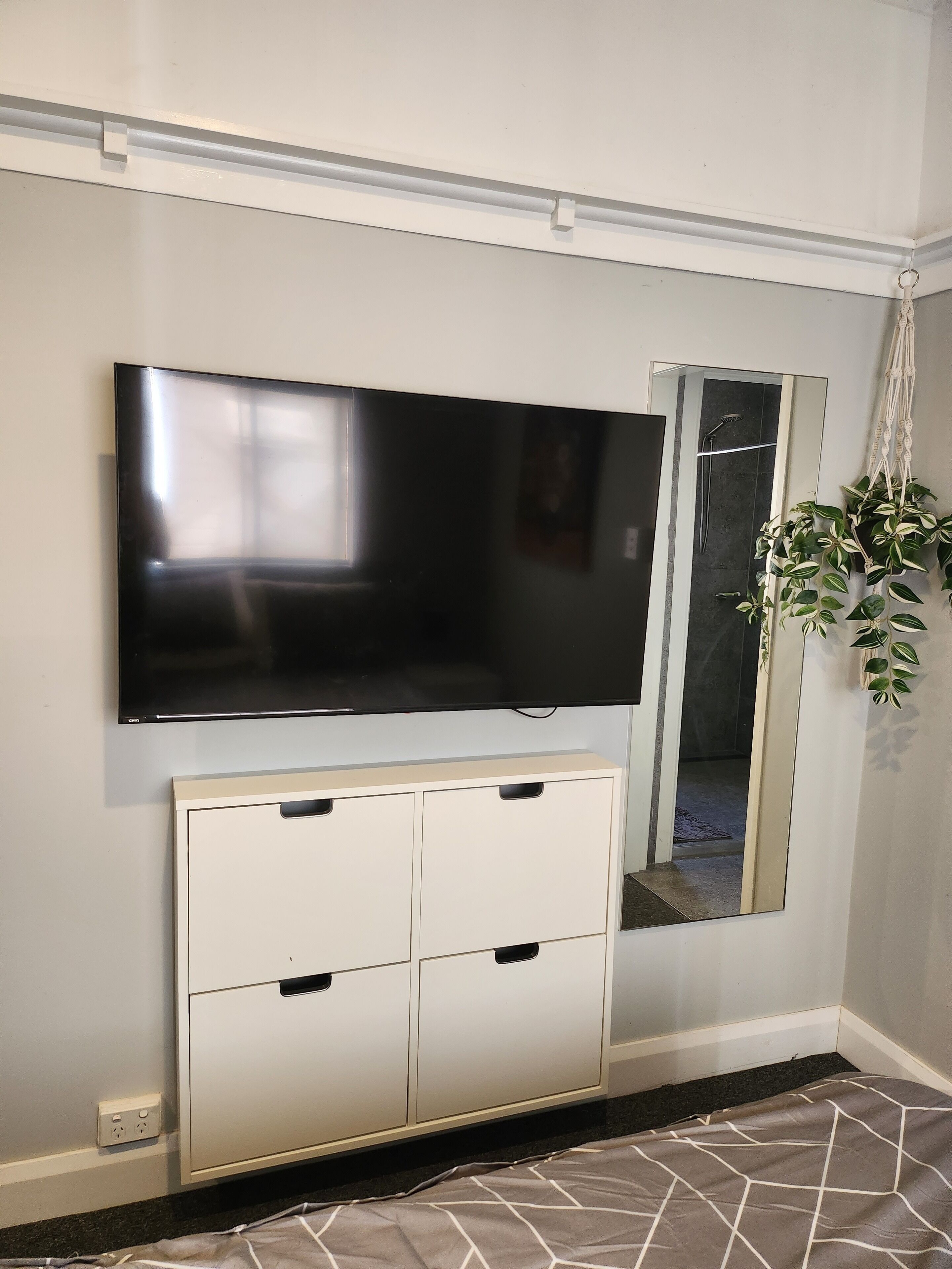 A flat-screen TV mounted on a wall, a mirror, and a cabinet with drawers.