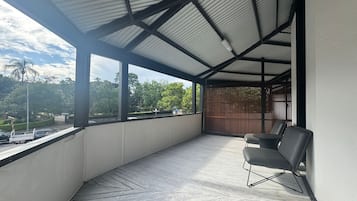 Un balcón techado con vistas a árboles y un vehículo estacionado.
