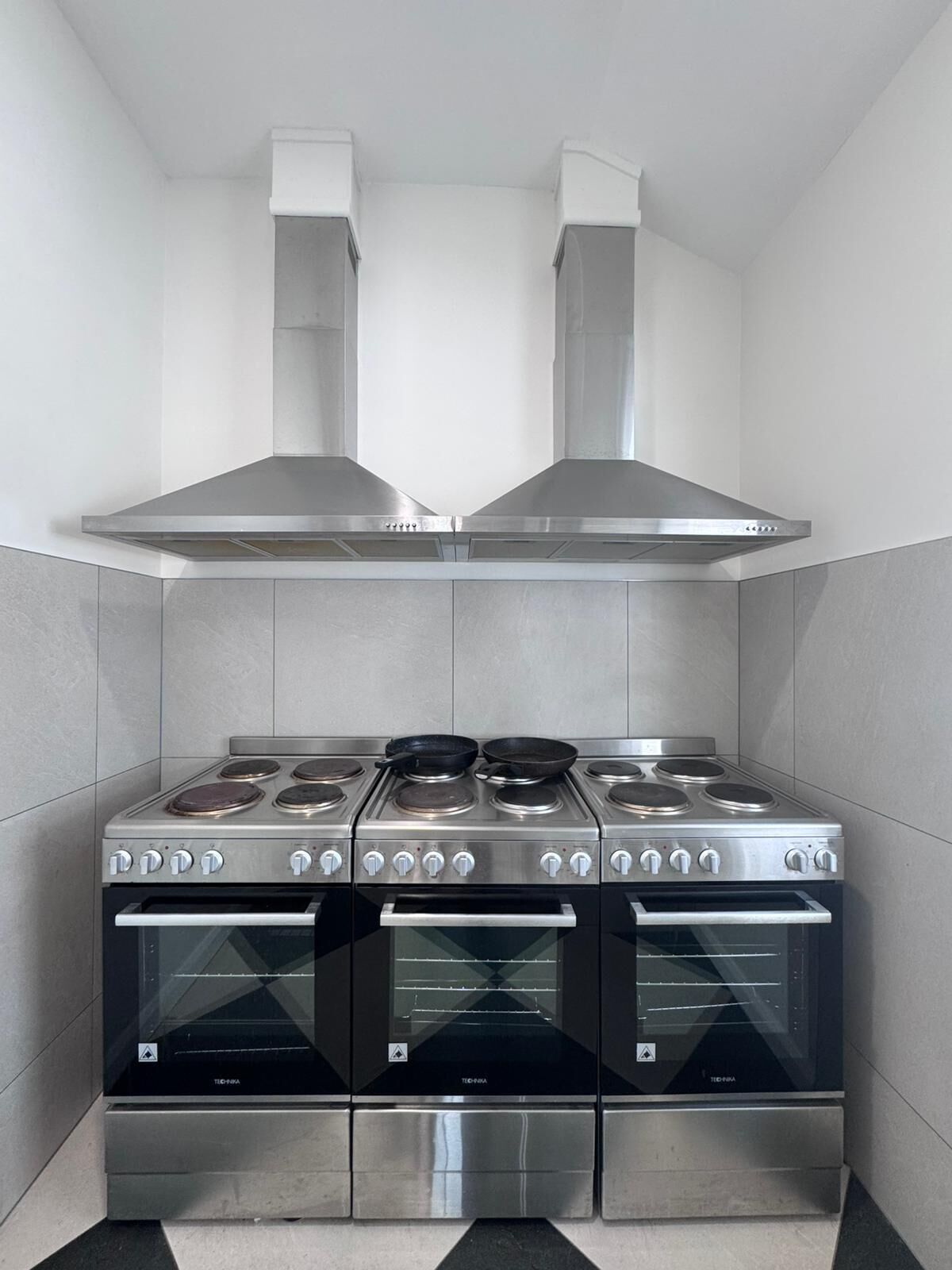 Une cuisine compacte équipée d’une cuisinière en acier inoxydable, de deux fours et d’une hotte aspirante.