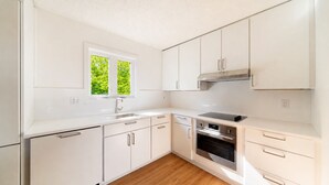 A modern kitchen with white cabinetry, a stainless steel oven, and a window with a view of greenery. - SNØFALL@CAMELBACK (Tannersville)