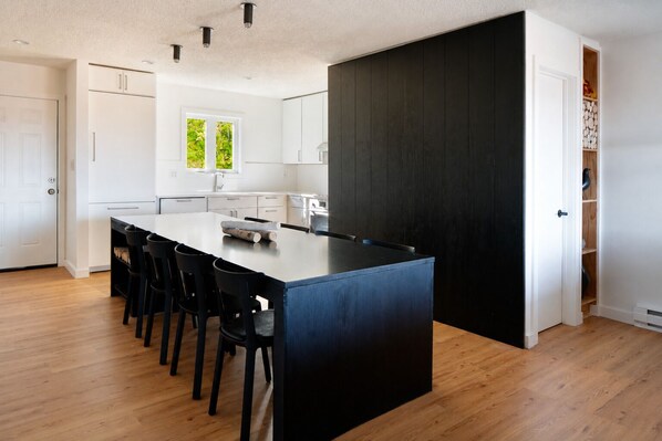 Une cuisine moderne dotée d’un îlot central, de chaises noires, de meubles blancs et d’un mur d’accent de couleur foncée.