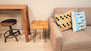 Una sala acogedora con una mesa de madera, un taburete pequeño y un sofá con cojines estampados.