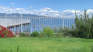 Un espacio cubierto de césped con una valla blanca y un muelle que se adentra en el agua.