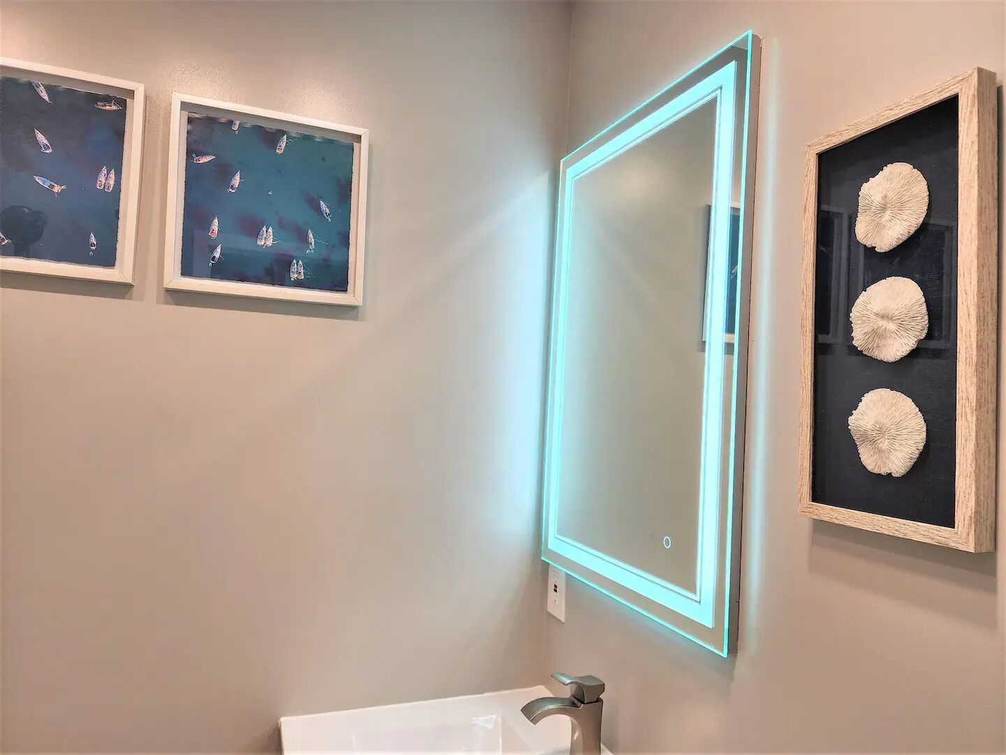 Un baño con un espejo, dos cuadros enmarcados y una estantería con objetos decorativos.
