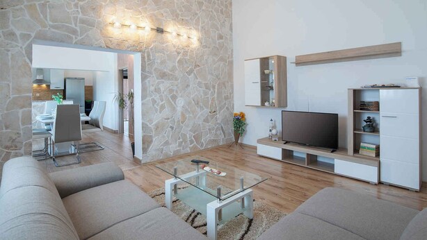 A modern living room with a stone accent wall, a flat-screen TV, and a dining area with a glass table. - Holiday apartment with air conditioning (Barban)