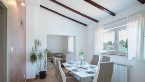 A dining area with a table set for four, a sofa in the background, and a window with curtains. - Holiday apartment with air conditioning (Barban)
