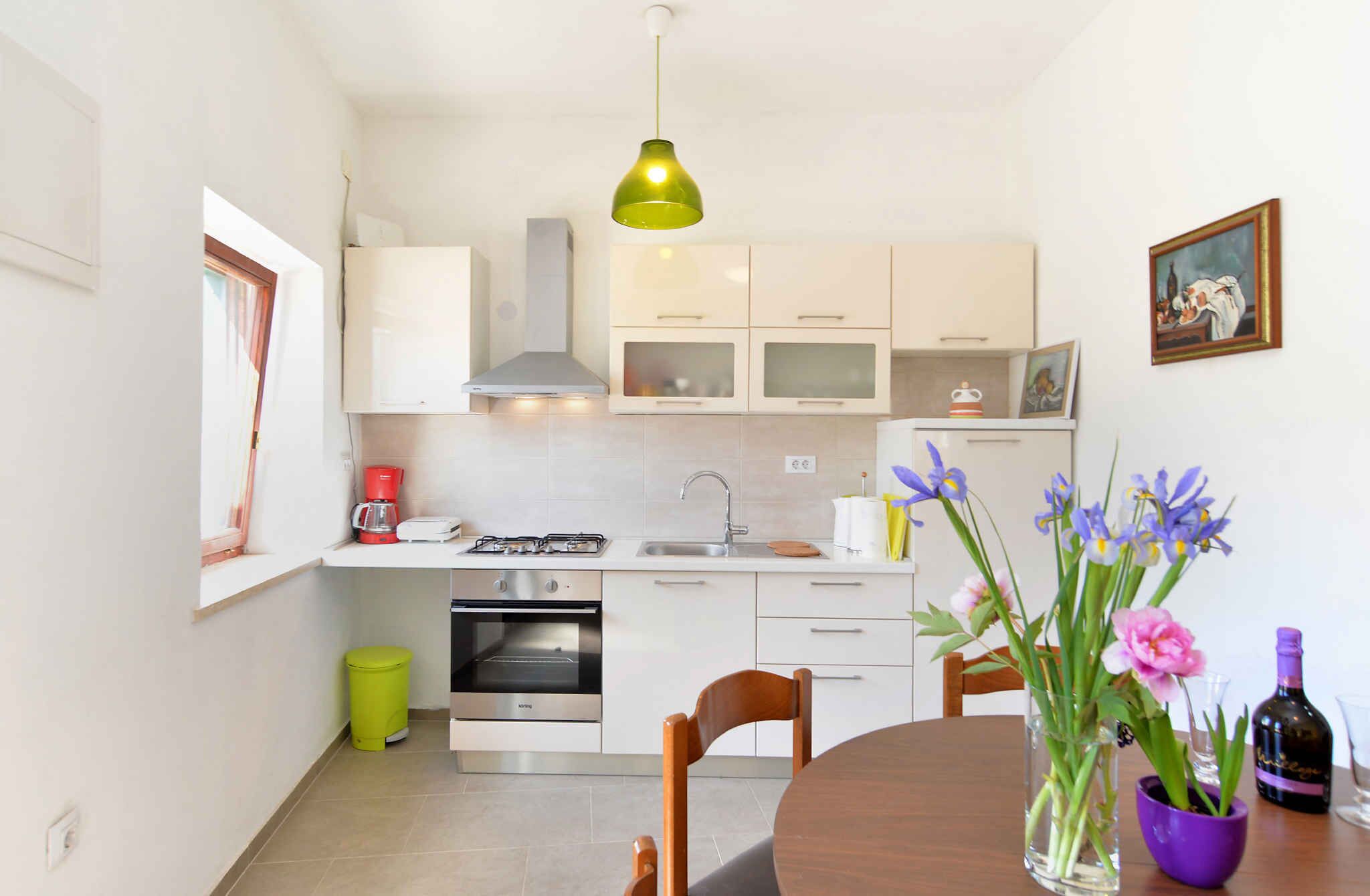A modern kitchen with white cabinets, a gas stove, a sink, and a dining area with a table and chairs.