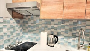 A kitchen with a modern design, featuring a stainless steel range hood, a black induction cooktop, a coffee maker, and a sink with a modern faucet.