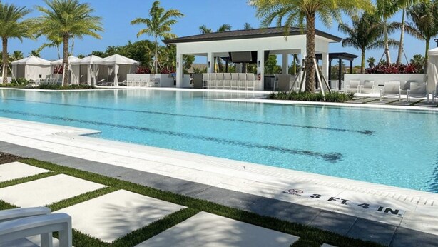 Una piscina con zona de estar cubierta, palmeras y cielo despejado.