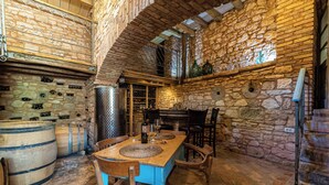 Una habitació rústica amb parets de pedra, taula i cadires de fusta, tones de vi i una prestatgeria per al vi.