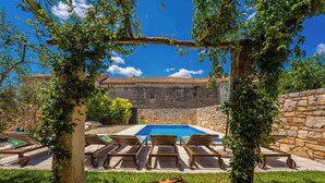 Edifici de pedra amb piscina, envoltat de gandules de fusta i una pérgola coberta de plantes enfilades.