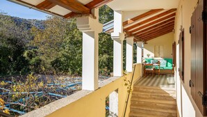 A covered outdoor area with a wooden ceiling, a staircase leading to a green sofa and table, and a view of a hillside with trees.