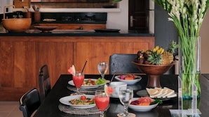 A dining area with a wooden table set for a meal, a painting on the wall, and a vase of flowers. - Legian 6BR Villa 16px Big Group Walk to 66 Beach (Bali)