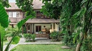 A two-story house with a porch, surrounded by lush greenery and a well-maintained lawn. - Legian 6BR Villa 16px Big Group Walk to 66 Beach (Bali)