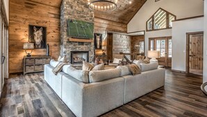 A spacious living room with a large sectional sofa, a stone fireplace, and a high ceiling with wooden beams. - Mountain Brooks Retreat - Hot Tub | Close to Downtown Blue Ridge | Outdoor Fireplace (Blue Ridge)