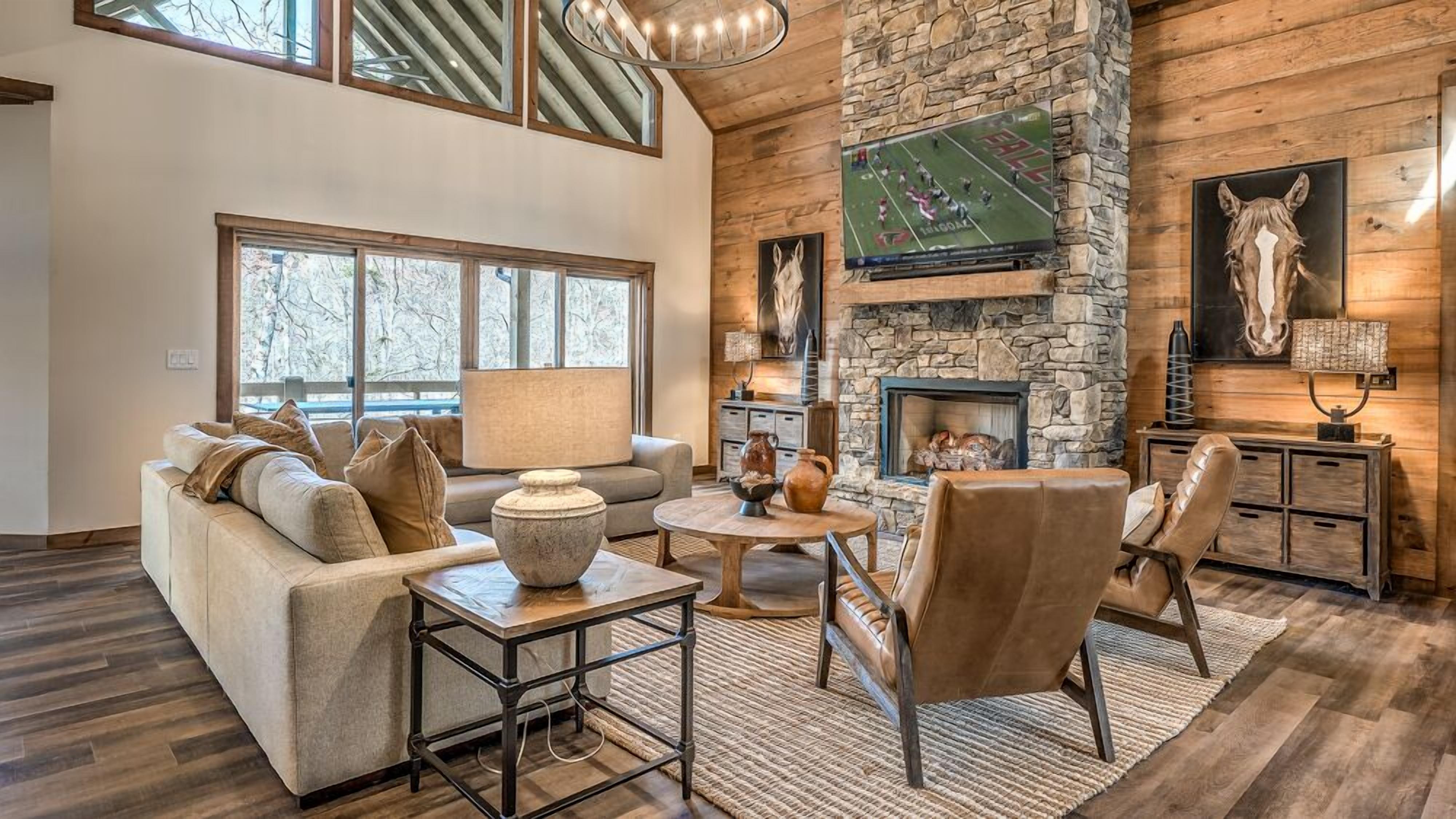 A spacious living room with a stone fireplace, a large window, and a mounted television.