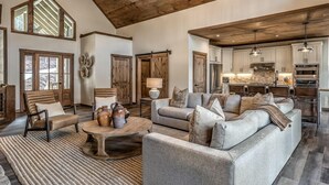 A spacious living room with a large grey sofa, a coffee table with vases, and a rustic wooden ceiling. - Mountain Brooks Retreat - Hot Tub | Close to Downtown Blue Ridge | Outdoor Fireplace (Blue Ridge)