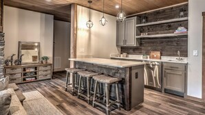 A modern kitchen with a bar area, wooden flooring, and a stone accent wall. - Mountain Brooks Retreat - Hot Tub | Close to Downtown Blue Ridge | Outdoor Fireplace (Blue Ridge)