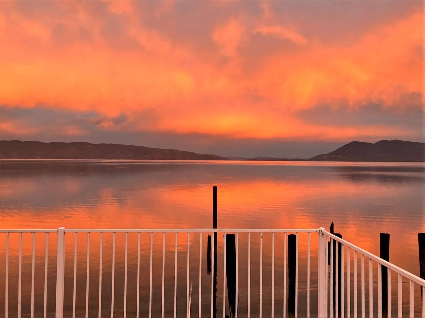 A calm lake with a sunset, a wooden dock, and distant hills.