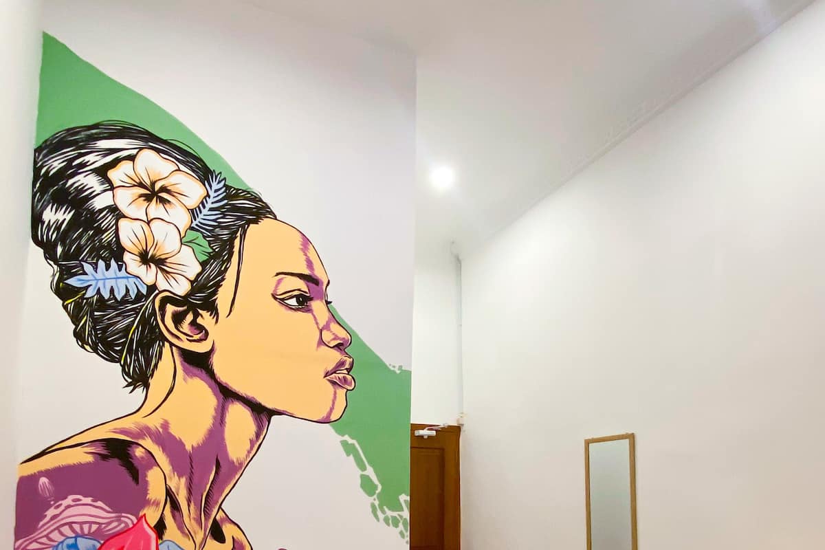 A hallway with a colorful mural on the wall, a wooden cabinet, and a mirror.