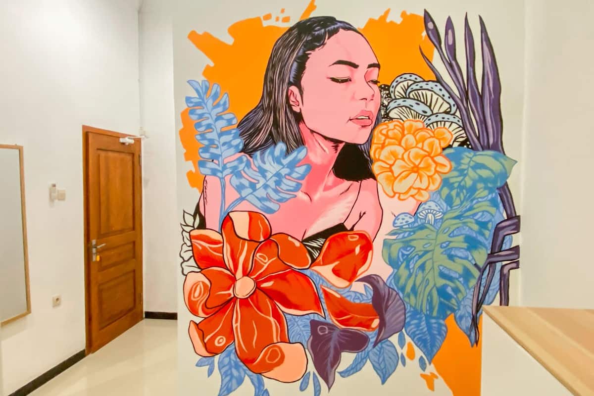 A hallway with a mural featuring a person surrounded by floral and leaf patterns.