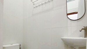 A small, clean bathroom with white tiles, a toilet, a sink, and a mirror. - ReVive by Snooze (Banyuwangi)