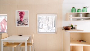 A modern kitchen with a white table, chairs, a window with a snowy view, and a shelf with jars.