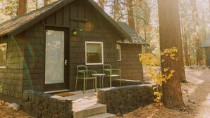 A cabin with a stone foundation, a door, a window, and two chairs outside.