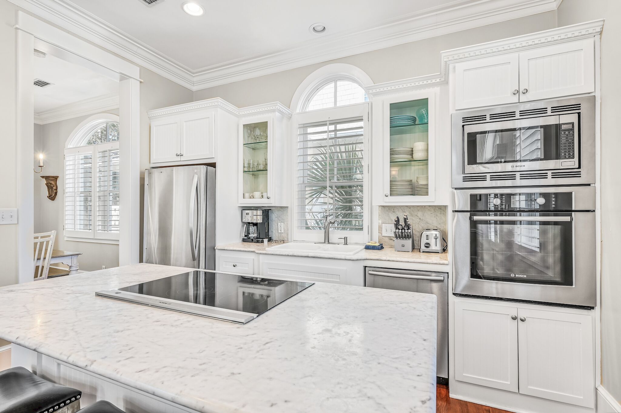 A modern kitchen with white cabinetry, a stainless steel refrigerator, a Bosch microwave, and an oven.