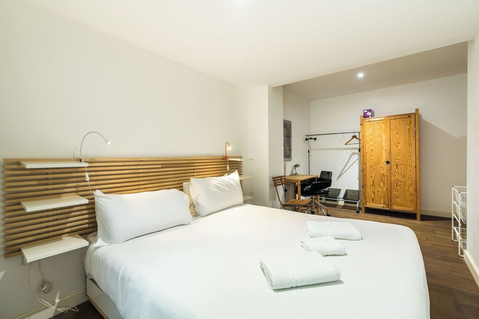 Een moderne hotelkamer met een houten hoofdbord, een bed met witte lakens, een bureau met stoel en een houten kledingkast.