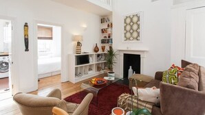 Amplia sala de estar con techo alto, chimenea, estantería y un área de descanso confortable.