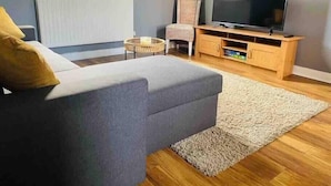 Un salon moderne avec un canapé gris, un meuble TV en bois et un grand téléviseur à écran plat.